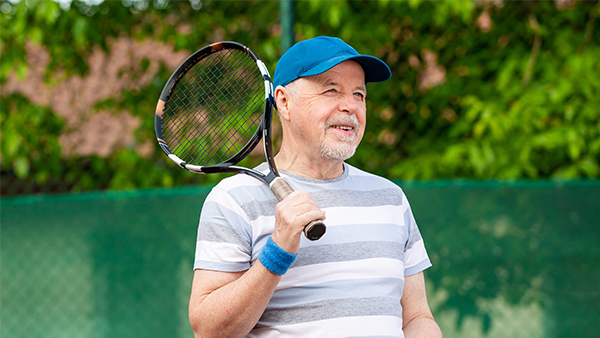 Middle aged man holding tennis racket, smiling